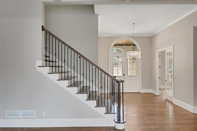 entryway with ornamental molding, wood finished floors, a chandelier, baseboards, and stairs