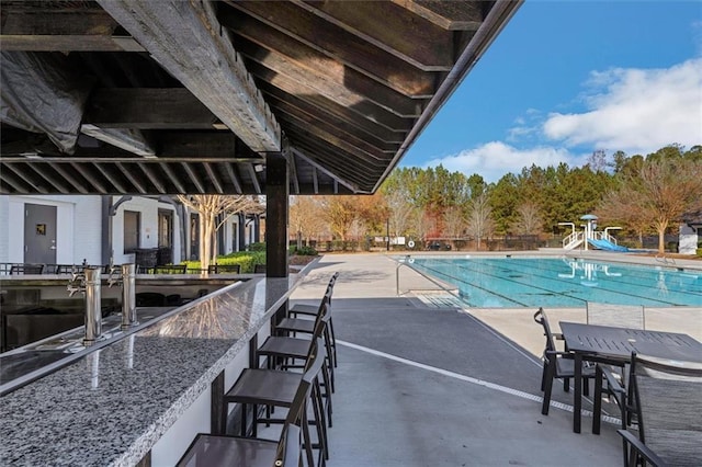 community pool with outdoor dry bar, a water slide, and a patio