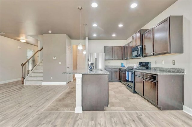 529 Dasheill Ln, Atlanta, GA 30349 - kitchen with appliances with stainless steel finishes, a kitchen island with sink, light stone counters, light wood-type flooring, and hanging light fixtures