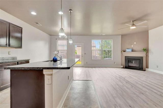 529 Dasheill Ln, Atlanta, GA 30349 - kitchen with a ceiling fan, a center island with sink, dark brown cabinetry, a fireplace with flush hearth, and light wood-style flooring