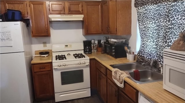 kitchen featuring a sink, brown cabinetry, white appliances, under cabinet range hood, and light countertops