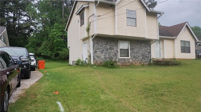 view of side of property with stone siding and a lawn