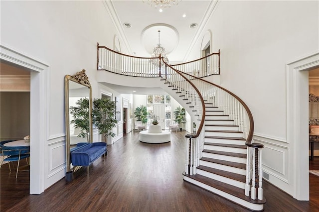 entrance foyer with dark wood-type flooring, ornamental molding, a chandelier, and a high ceiling