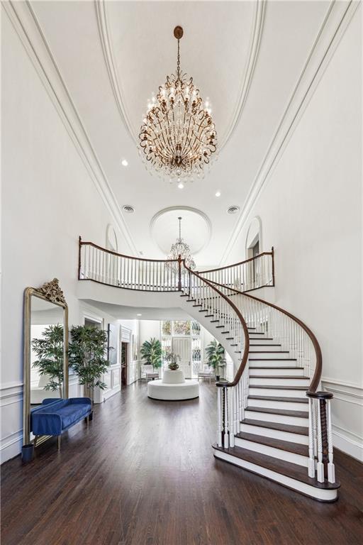 stairs featuring an inviting chandelier, crown molding, wood-type flooring, a raised ceiling, and a towering ceiling