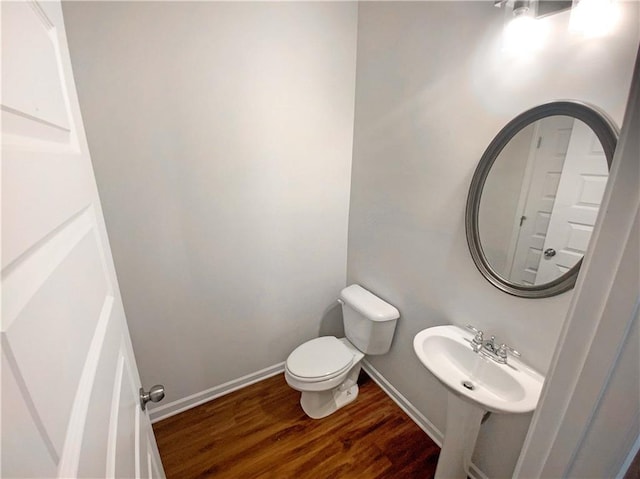 bathroom featuring toilet, wood finished floors, baseboards, and a sink