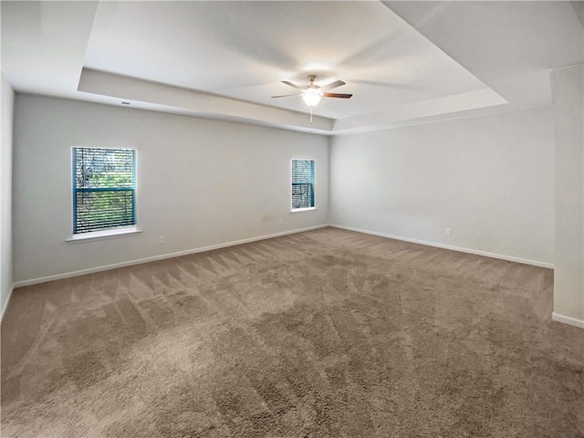 empty room with a tray ceiling, baseboards, ceiling fan, and carpet flooring