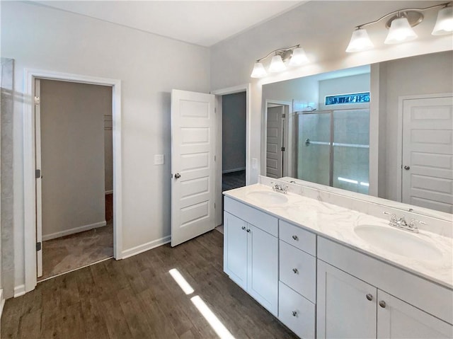 bathroom featuring double vanity, a shower stall, wood finished floors, and a sink