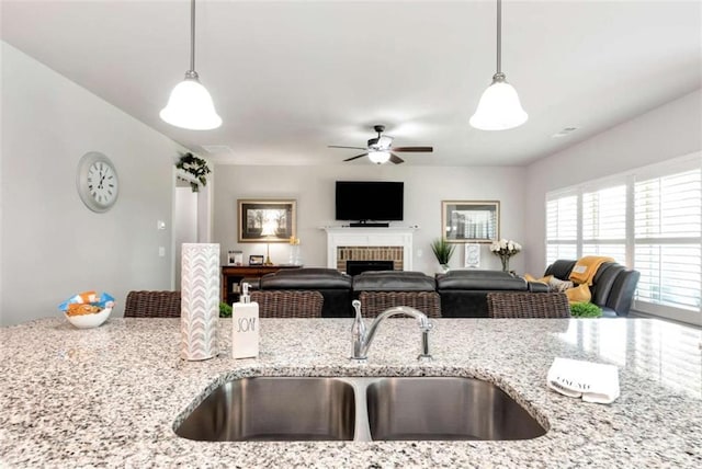 1311 Calgary Lk, Winder, GA 30680 - kitchen featuring a ceiling fan, hanging light fixtures, a brick fireplace, and light stone counters