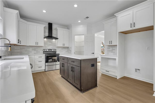 kitchen with white cabinets, electric range, wall chimney exhaust hood, and a kitchen island