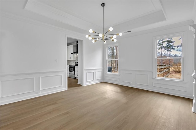 unfurnished dining area with crown molding, a notable chandelier, a tray ceiling, and wood-type flooring