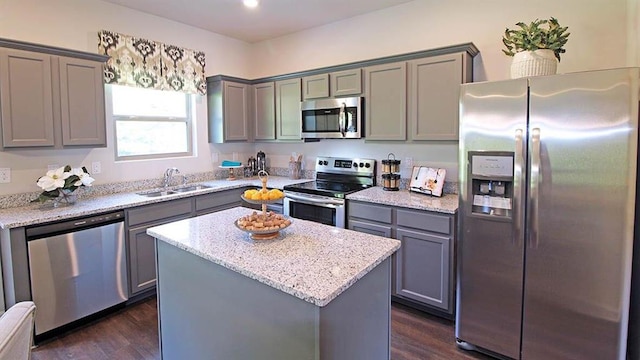 kitchen with a center island, sink, light stone counters, appliances with stainless steel finishes, and dark hardwood / wood-style flooring