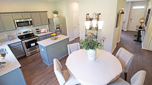 kitchen with light stone countertops, a center island, dark hardwood / wood-style floors, decorative light fixtures, and appliances with stainless steel finishes