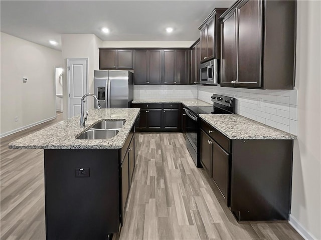kitchen featuring appliances with stainless steel finishes, a kitchen island with sink, decorative backsplash, light wood finished floors, and a sink