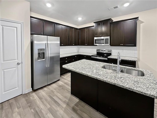 kitchen with light stone counters, sink, a center island with sink, stainless steel appliances, and light hardwood / wood-style floors