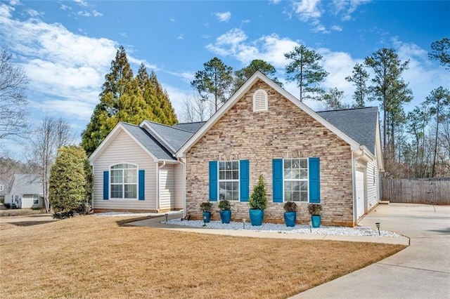 view of front of house with concrete driveway, stone siding, an attached garage, fence, and a front lawn