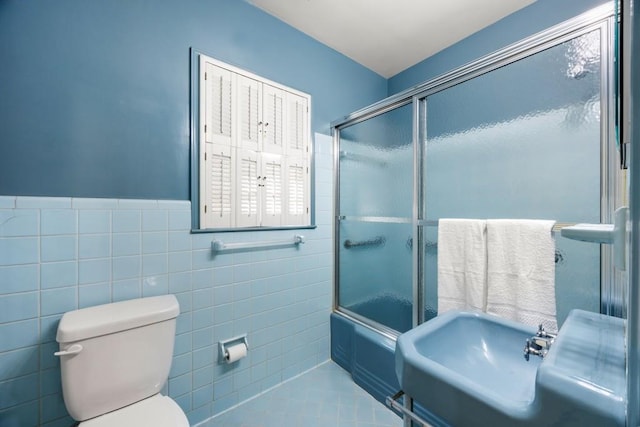 bathroom featuring toilet, combined bath / shower with glass door, tile walls, and tile patterned flooring