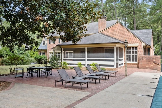 rear view of property with a sunroom, a lawn, and a patio