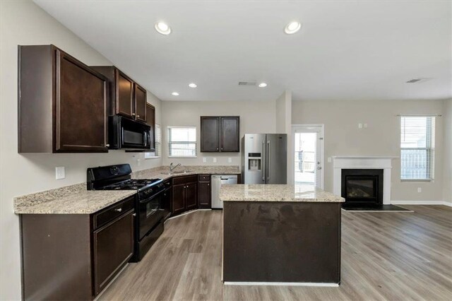 kitchen with light stone countertops, light hardwood / wood-style flooring, sink, black appliances, and dark brown cabinetry