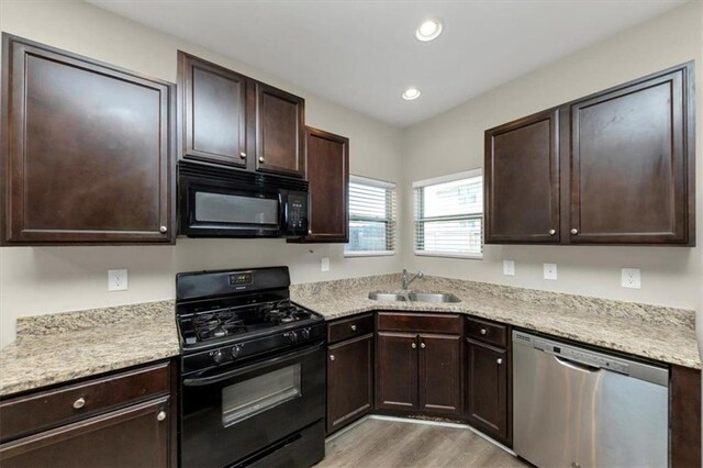 kitchen featuring sink, decorative light fixtures, a center island, light stone counters, and black appliances