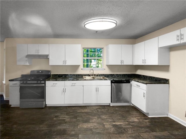 kitchen with a textured ceiling, appliances with stainless steel finishes, white cabinetry, dark stone counters, and sink