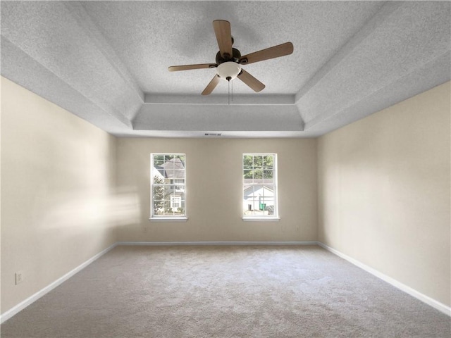 spare room with a textured ceiling, carpet flooring, ceiling fan, and a raised ceiling