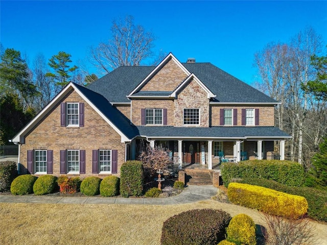 view of front of property with covered porch, a chimney, and brick siding