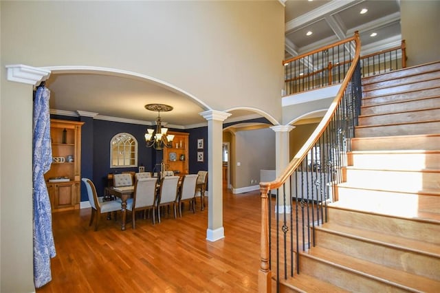 staircase with arched walkways, wood finished floors, a towering ceiling, ornamental molding, and decorative columns