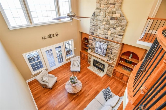 living room featuring built in features, wood finished floors, a stone fireplace, and stairs