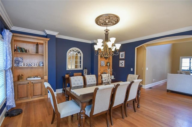 dining room featuring arched walkways, an inviting chandelier, ornamental molding, wood finished floors, and baseboards