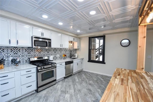 kitchen featuring light wood finished floors, decorative backsplash, an ornate ceiling, appliances with stainless steel finishes, and white cabinetry