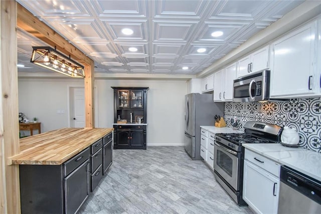 kitchen with an ornate ceiling, stainless steel appliances, wooden counters, backsplash, and white cabinetry