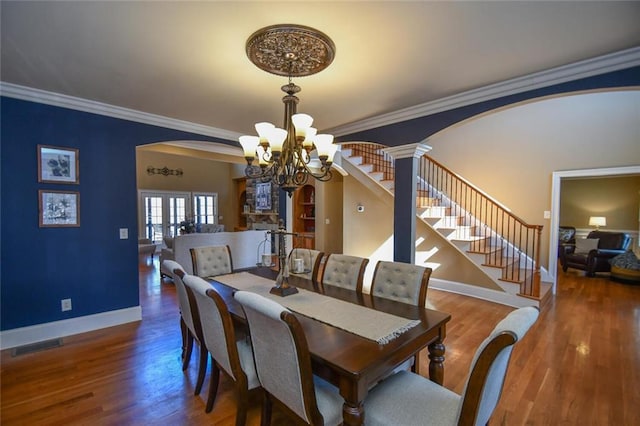 dining room with visible vents, arched walkways, ornamental molding, wood finished floors, and stairs