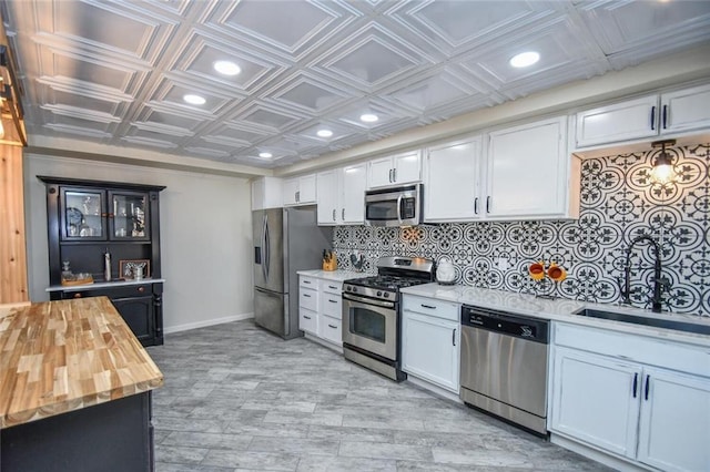 kitchen featuring stainless steel appliances, butcher block counters, white cabinetry, tasteful backsplash, and an ornate ceiling