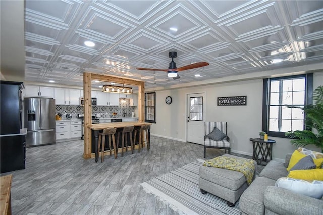 living area featuring recessed lighting, a ceiling fan, baseboards, light wood finished floors, and an ornate ceiling