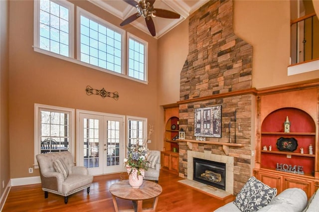 living area featuring built in shelves, french doors, a stone fireplace, wood finished floors, and baseboards