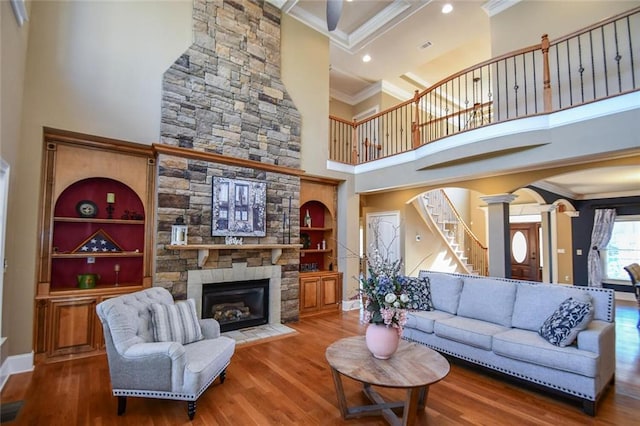 living room with arched walkways, ornamental molding, a stone fireplace, wood finished floors, and ornate columns