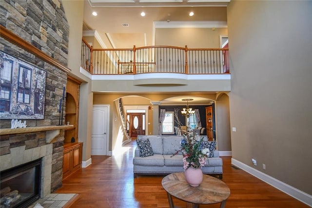 living room featuring arched walkways, a fireplace, wood finished floors, baseboards, and an inviting chandelier