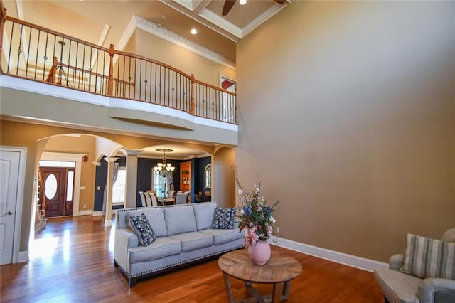 living room featuring crown molding, baseboards, a high ceiling, wood finished floors, and ornate columns