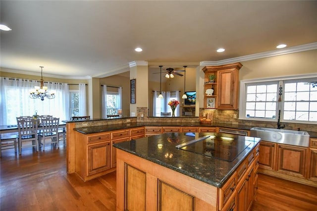 kitchen with black electric stovetop, brown cabinetry, a sink, and a center island