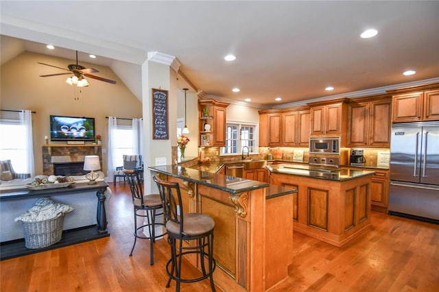 kitchen featuring open shelves, brown cabinetry, open floor plan, built in appliances, and dark stone counters