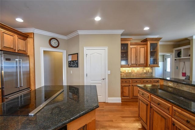 kitchen with black electric stovetop, backsplash, brown cabinetry, light wood-type flooring, and built in refrigerator