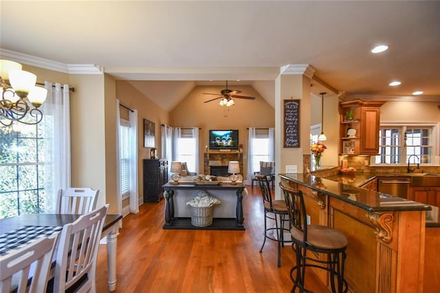 kitchen featuring ceiling fan with notable chandelier, a fireplace, wood finished floors, brown cabinets, and plenty of natural light