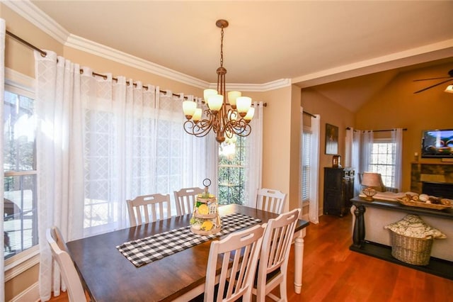 dining area featuring lofted ceiling, ceiling fan with notable chandelier, a fireplace, wood finished floors, and ornamental molding