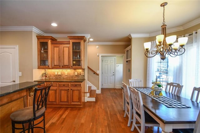 dining space featuring crown molding, stairway, an inviting chandelier, and wood finished floors