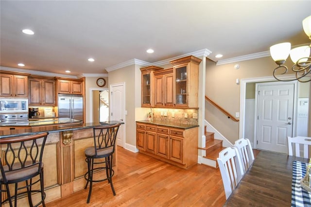 kitchen featuring a kitchen bar, brown cabinets, backsplash, and built in appliances