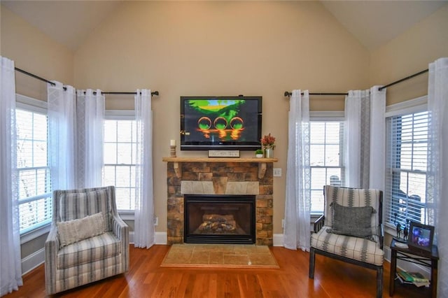 living area with vaulted ceiling, a fireplace, wood finished floors, and baseboards