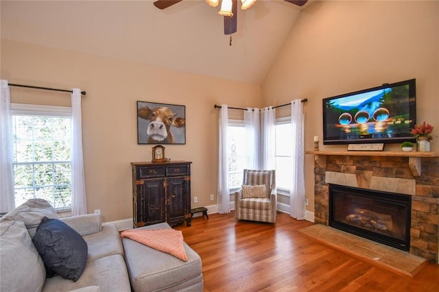 living room with high vaulted ceiling, a fireplace, wood finished floors, a ceiling fan, and baseboards