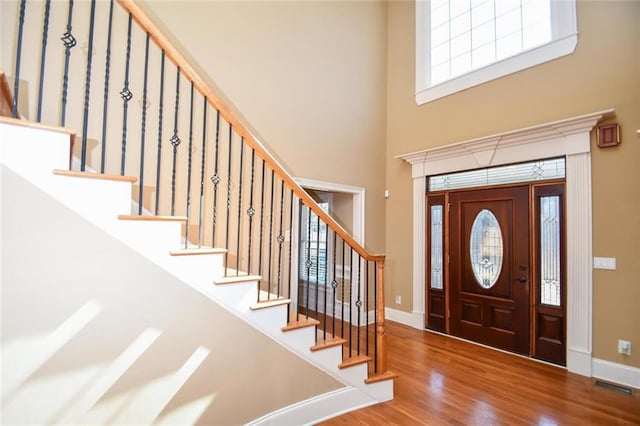 entrance foyer with a towering ceiling, visible vents, baseboards, and wood finished floors