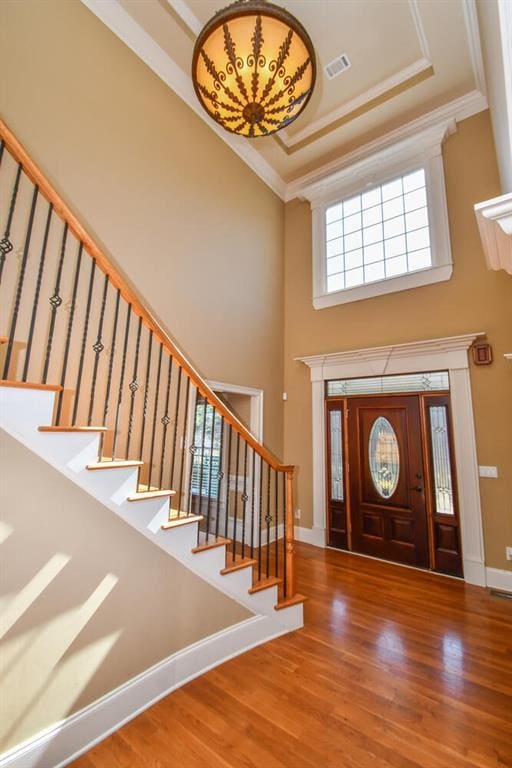 foyer with wood finished floors, visible vents, a towering ceiling, baseboards, and ornamental molding