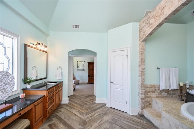 bathroom with vaulted ceiling, a wealth of natural light, a relaxing tiled tub, and visible vents